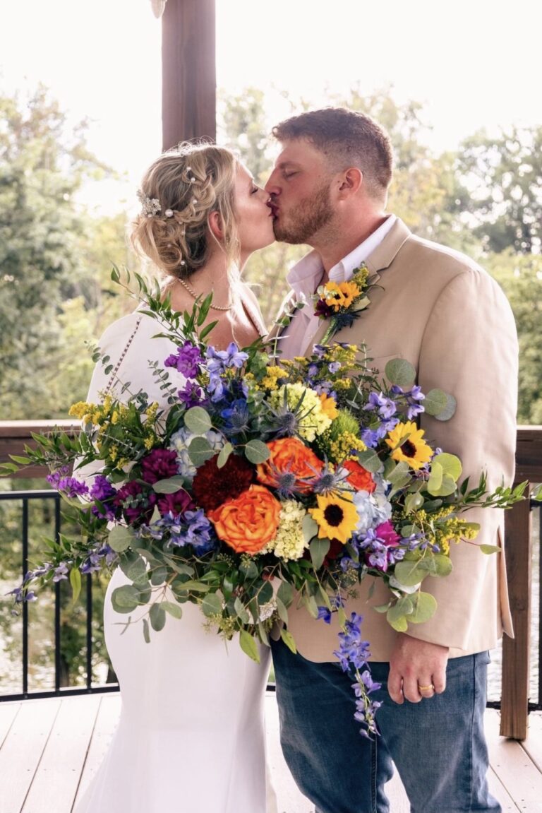 Bride and groom share a kiss with a vibrant bouquet in the foreground.