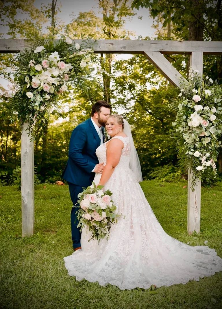 Bride and groom sharing a kiss under a floral arch outdoors.