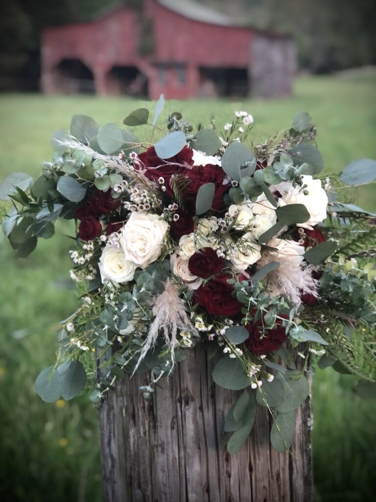 Rustic floral arrangement with deep red and white flowers on a wooden stump.