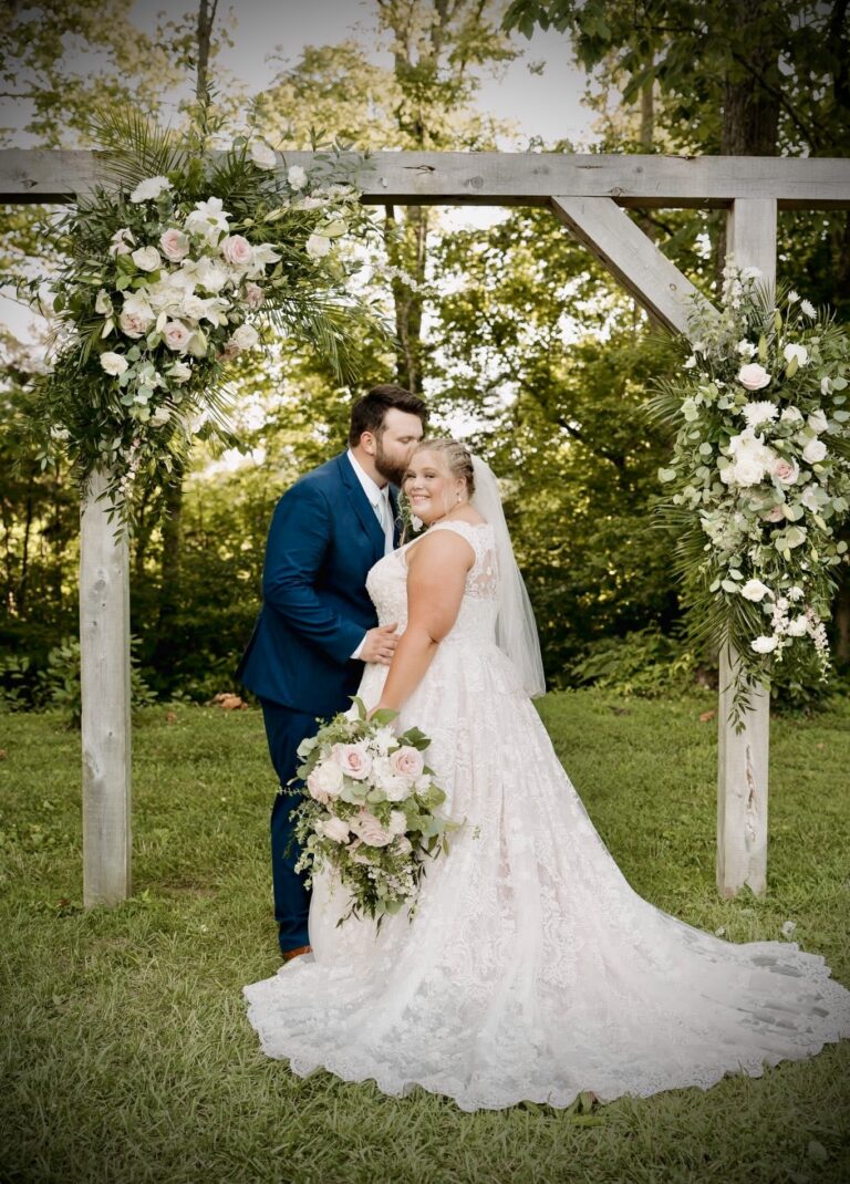 Bride and groom share a kiss under a floral arch at their outdoor wedding.
