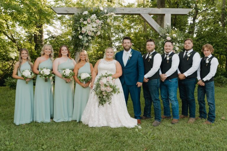 A wedding party posing outdoors with the bride and groom at the center.