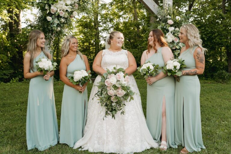Bride and bridesmaids in pastel green dresses holding bouquets outdoors.