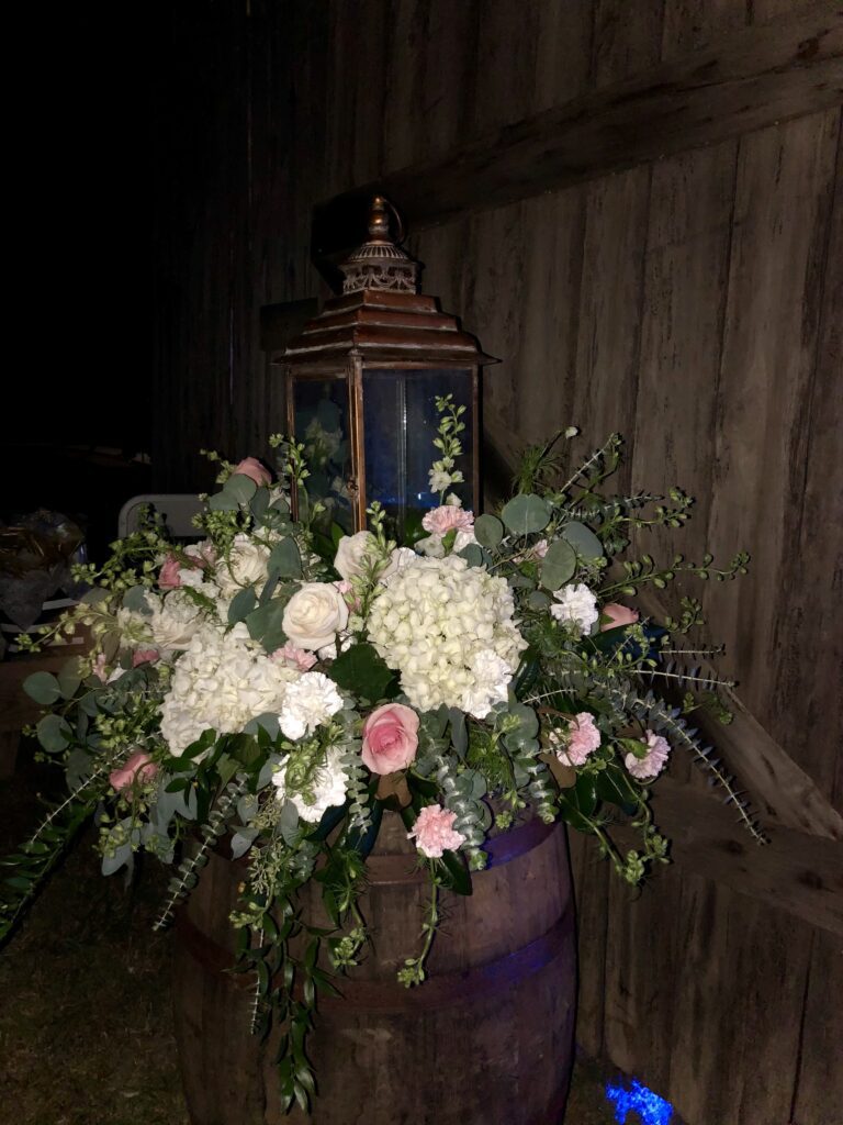 A lantern surrounded by a lush floral arrangement with white and pink flowers.