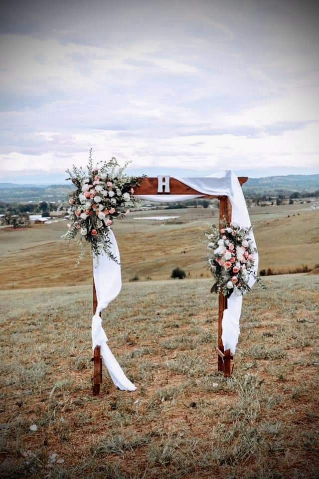 Rustic wedding arch adorned with flowers in an open field.