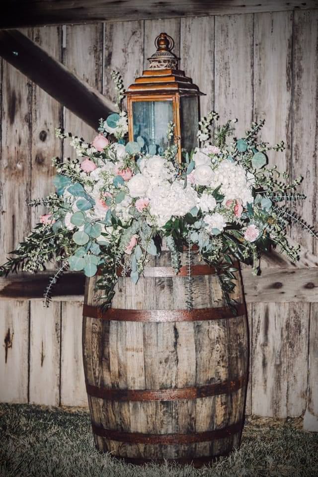Rustic wooden barrel with a lantern and a floral arrangement in front of a weathered wooden wall.