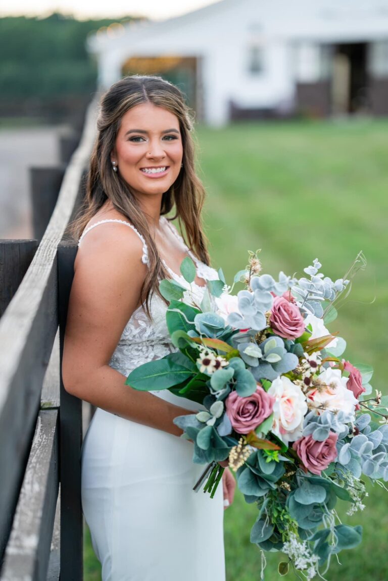 Bride in white dress holding a large bouquet outdoors.