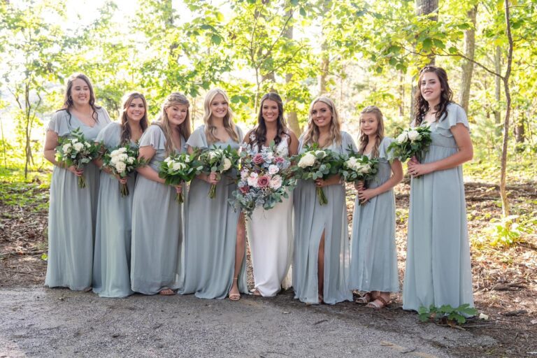 Bride with bridesmaids in light blue dresses holding bouquets outdoors.