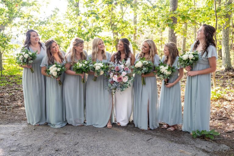 Bride with bridesmaids in light gray dresses holding bouquets outdoors.