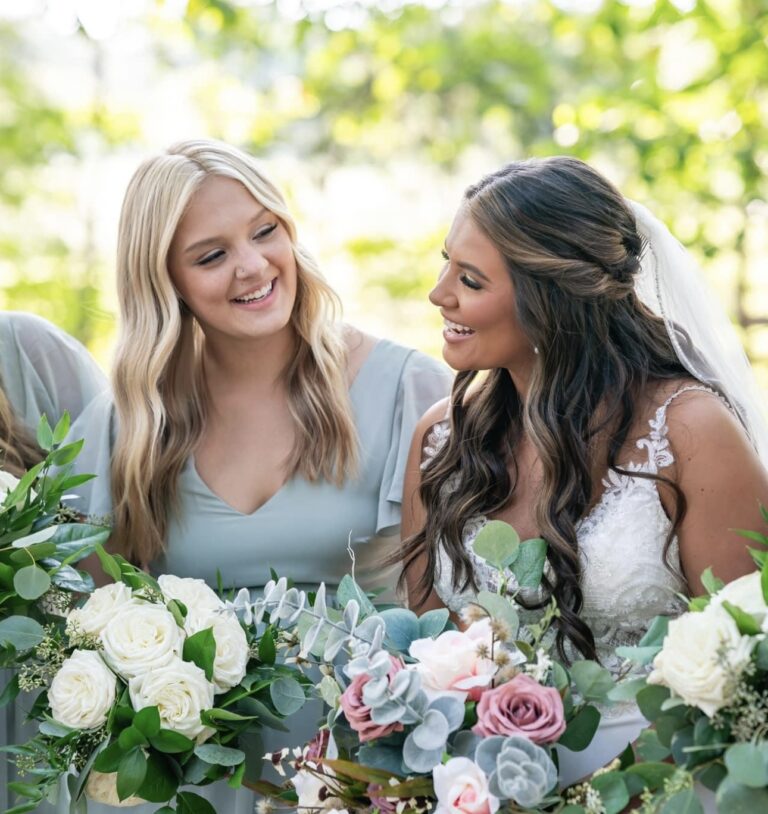 Two women smiling and enjoying a moment at a floral-decorated event.