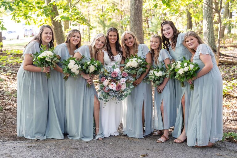 Bridesmaids in light blue dresses holding bouquets and smiling outdoors.