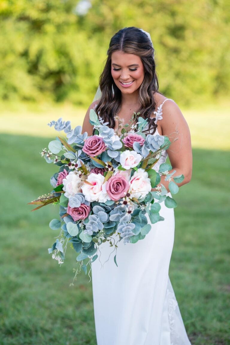 Bride holding a large, colorful floral bouquet outdoors.