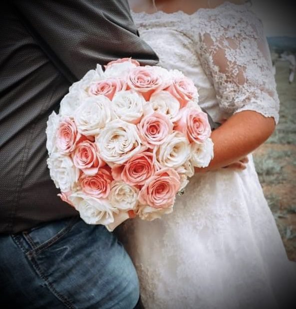 Bride holding a bouquet of pink and white roses embracing someone.
