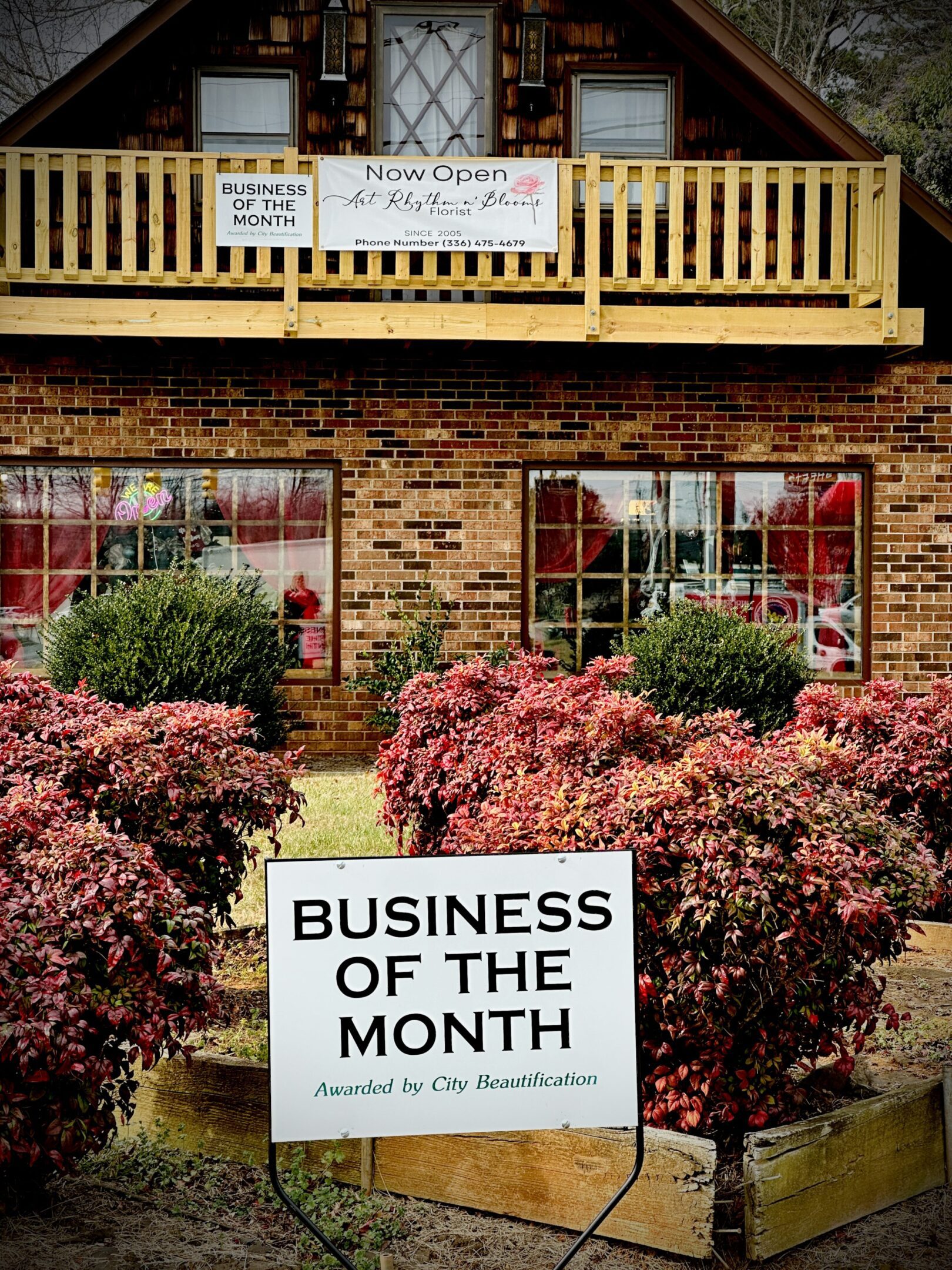 A storefront with a "Business of the Month" sign and colorful shrubs.